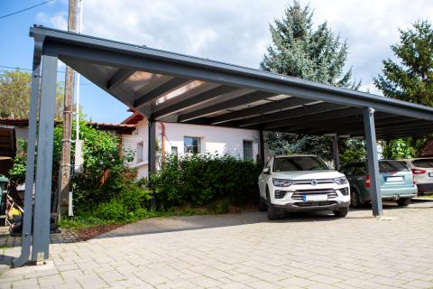 Napelemekkel fedett, extra hosszú, négy állásos kocsibeálló rétegragasztott fa szerkezettel.